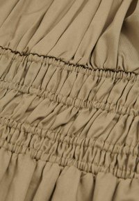 Beige stof met smock-stiksel, met een geplooide textuur en verticale plooien. Zacht en licht materiaal met een gladde afwerking.