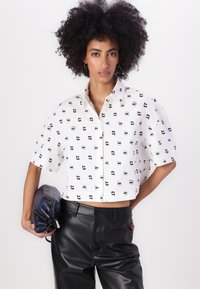 Kuttet hvit skjorte med svart grafisk mønster, kort ermene og spiss krage. Kombinert med svarte imitation lærebukser og en brettet clutch.