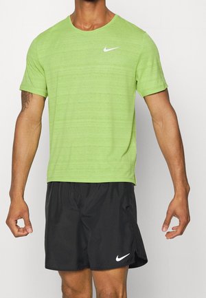 Homme portant un t-shirt de sport Nike à manches courtes vert vif et un short de course Nike noir, debout les bras légèrement écartés.