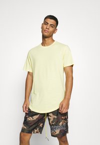 Helles gelbes T-Shirt mit kurzen Ärmeln und Rundhalsausschnitt, kombiniert mit Camouflage-Print-Shorts mit elastischem Bund und Kordelzug.