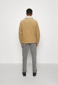 Beżowa kurtka z corduroyu z białym kołnierzem z owczej wełny, w połączeniu z szarymi spodniami cargo i czarnymi butami, widziana z tyłu.