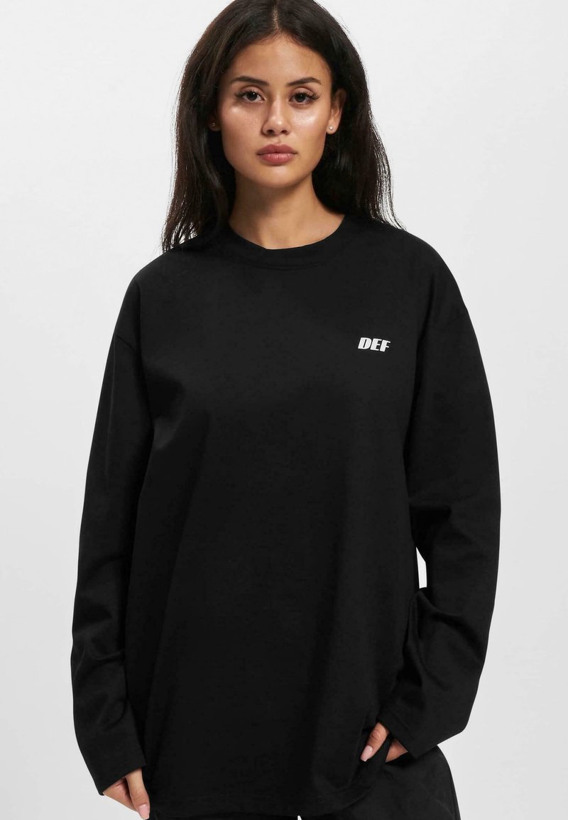 Black long-sleeve t-shirt made of soft fabric, featuring a white "DEF" logo on the left chest. Relaxed fit with dropped shoulders.