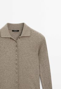 Chemise en maille côtelée beige à manches longues avec col et rangée de boutons sur le devant.