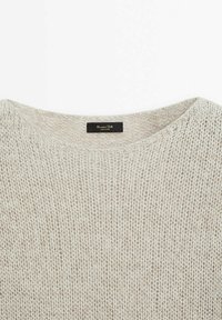 Pull gris clair en tricot avec un col rond. Présente un tissage texturé et une étiquette noire avec un texte blanc à l'intérieur.