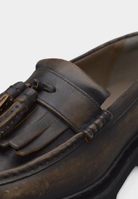 Καφέ δερμάτινα μοκασίνια με φούντες και διακοσμητικές λεπτομέρειες με κρόσσια, που παρουσιάζουν υφασμένη ραφή και ομαλή εσωτερική επένδυση.