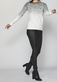 Pull blanc avec dégradé noir et paillettes, associé à un pantalon en cuir noir moulant et des bottines à talons noires.