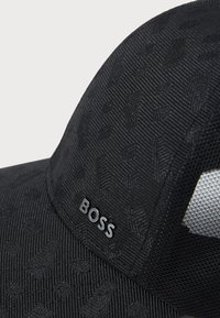 Casquette noire en tissu texturé avec un motif subtil. Accompagnée d'une étiquette de logo brillante pour la marque. Panneaux en maille pour une meilleure respirabilité.
