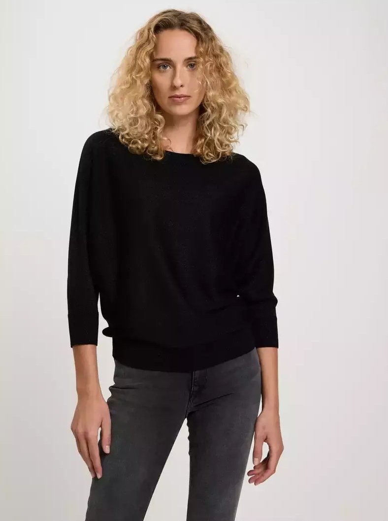 Czarny sweter z dzianiny o szerokim dekolcie, rękawach nietoperzowych i dopasowanym dole. Nosi się z ciemnoszarymi dżinsami. Gładka tekstura, luźny krój.