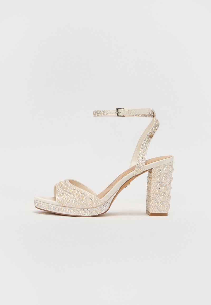 Sandale à talon beige avec bride à la cheville, bout ouvert, décorée de perles et de strass sur le talon et les brides.