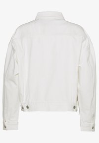 Achteraanzicht van een eenvoudige witdenimjack met lange mouwen, geknoopte manchetten en verstelbare zijtabs met metalen knopen.