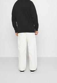 Svart sweatshirt med avslappnad passform, i kombination med vita cargobyxor med sidfickor. Outfiten kompletteras av svartvita sneakers.