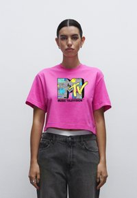 Lyserød cropped t-shirt med et multicolor MTV-logo i struktureret design. Sammen med grå højtaljede jeans. Enkel, afslappet stil.