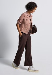 En ljusrosa jeansjacka med två bröstfickor, bruna vida byxor och vita sneakers med beige och silverdetaljer.