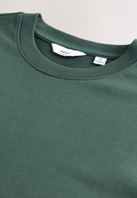 Dark green crew neck t-shirt made of soft cotton blend fabric. Features a relaxed fit with a smooth texture and labeled interior tag.