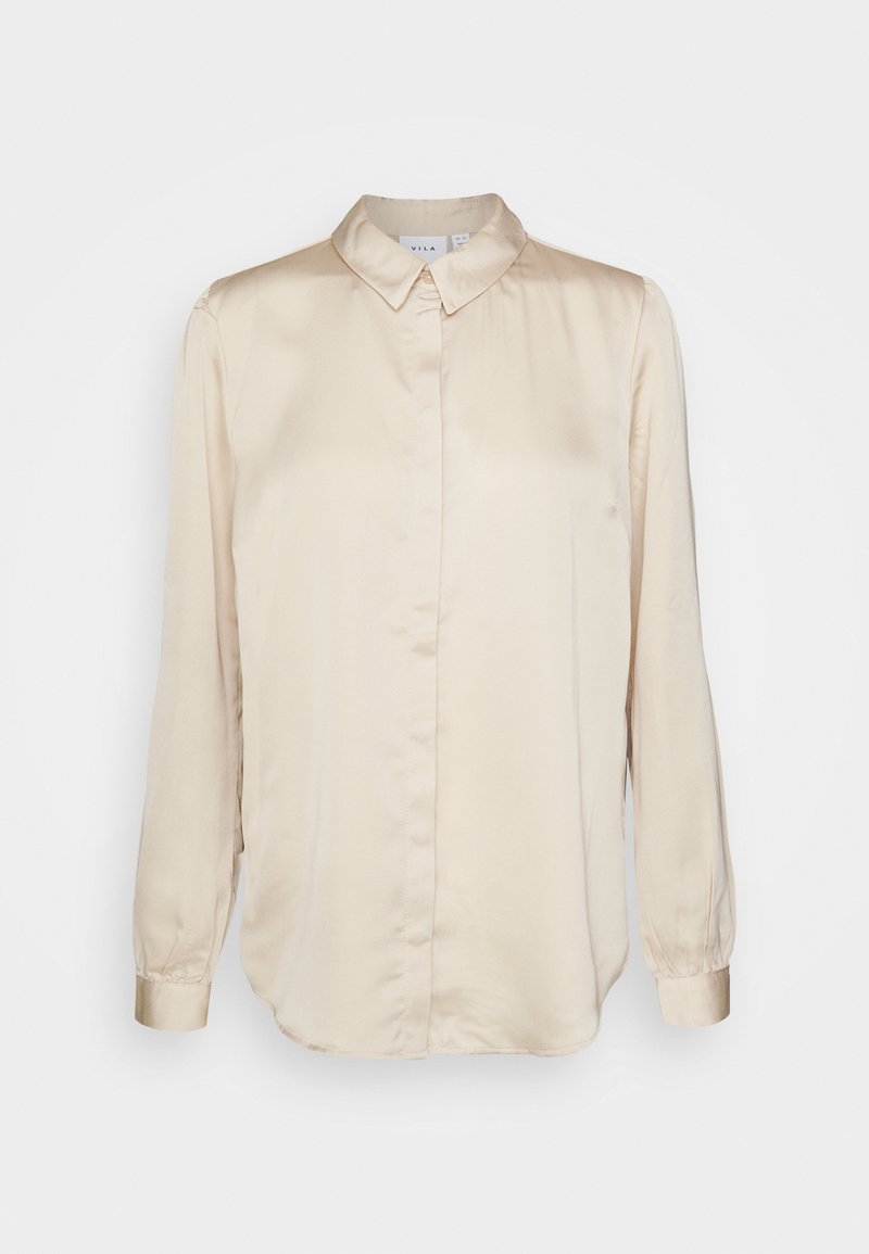 Blouse en satin beige à manches longues, col classique et coupe droite. Dotée de poignets boutonnés et d'un léger éclat.