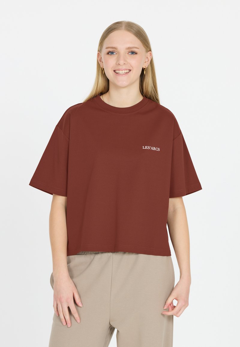 Mörkröd kortärmad t-shirt med ribbad rund halsringning, har vit text "LES'ARCS" på vänster sida. Slät tygtextur.