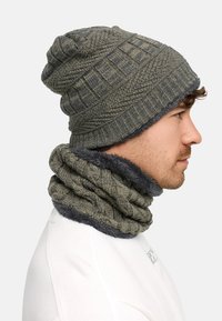 Knitted beanie in olive green with textured pattern. Coordinating grey fleece-lined neck warmer. Both accessories are layered and cozy.