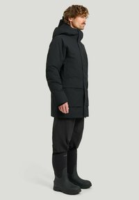 Svart vattentät parkas med huva, sidofickor och rak snitt. Kombinerat med svarta gummistövlar och stiliga svarta byxor.