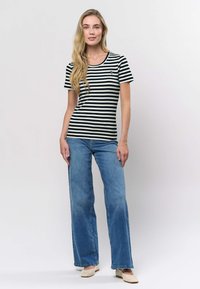 Mustavalkoraidallinen lyhythihainen paita yhdistetty vaaleansinisiin leveälahkeisiin farkkuihin. Malli käyttää beigenvärisiä punottuja kenkiä. Yksinkertainen ja klassinen malli.