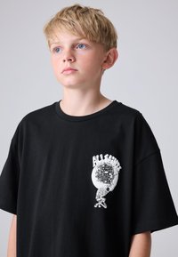 Fekete pamut póló nagy fehér diszkógömb grafikával és az "ALL SAINTS" felirattal a bal mellrészen. Laza szabás, rövid ujjú.