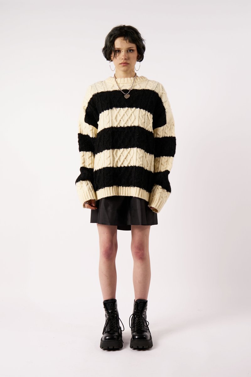 Juoda ir kreminė juostelėmis megzta stora megztinė su pynių raštu. Suderinta su juoda sijonu ir juodais batų lygiais kovos batais.