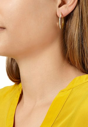 Gold hoop earring with a smooth, shiny finish, featuring a small row of clear stones along the edge. Worn in a close-up profile view.