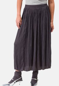 Gonnona midi plissettata grigio scuro con vita elastica, abbinata a scarpe con tacco argentate e calze grigie a coste. Tessuto leggero con texture.