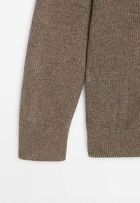 Poignets de pull en maille côtelée marron avec texture visible et ourlet plié sur un fond blanc.