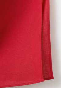 Tissu en lin rouge avec coutures visibles et ourlet, légèrement plié sur le côté droit sur un fond blanc.