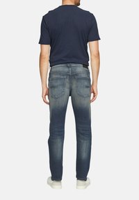 T-shirt bleu marine associé à un jean délavé avec une coupe droite, des poches standard et des baskets blanches sur un fond uni.