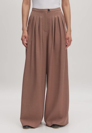 Lichtbruine, wijde broek met diepe plooien aan de voorkant, een op maat gemaakte pasvorm en een enkele knoopsluiting in de taille. Soepele stofstructuur.