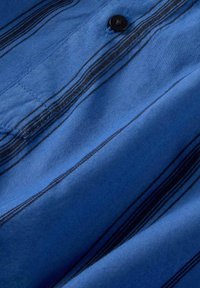 Tessuto blu con righe orizzontali nere, caratterizzato da un bottone nero e una texture morbida, adatto per un abbigliamento casual.