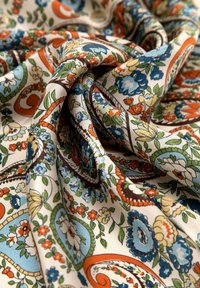 Tessuto di cotone con intricati motivi floreali e paisley in blu, arancione e verde su uno sfondo crema, contraddistinto da una texture liscia.