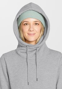 Sudadera gris heather con cuello drapeado y cordones, combinada con un gorro de punto en azul claro. Logo bordado sutil en el pecho.
