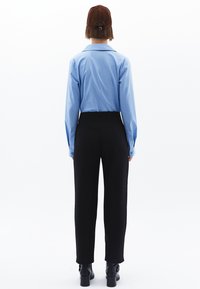 Světle modrá košile s dlouhým rukávem a límečkem, kombinovaná s černými kalhotami s vysokým pasem a černými kotníkovými botami, viděná zezadu.
