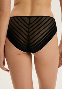 Czarne siateczkowe majtki z wzorem zygzakowym, z przezroczystymi paskami, połączone z nieprzezroczystym materiałem wzdłuż brzegów dla kontrastu i tekstury.