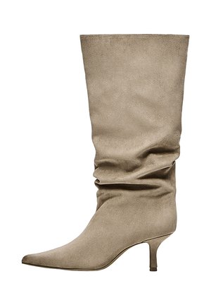 Bottes beige en suède mi-mollet amples avec bout pointu et petit talon kitten bas, orientées vers la gauche sur fond blanc.