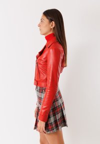 Giacca cropped in pelle rossa con zip, abbinata a una gonna a quadri con motivi grigi, rossi e neri. Tessuto liscio, design aderente.