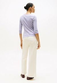 Lila gestreiftes Langarmhemd, kombiniert mit kremfarbenen weit geschnittenen Hosen. Das Hemd hat einen runden Ausschnitt und sitzt eng.