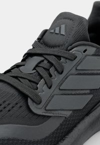 Black athletic shoe featuring a textured upper, sleek design, prominent laces, and three stripes branding on the side with a matte finish.