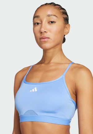 Light blue sports bra with thin straps, rounded neckline, and a mesh panel. Features a white logo accent on the front. Made of stretchy material.