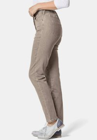 Beige schmale Jeans mit elastischem Bund, zwei Gesäßtaschen und einer glatten Textur, kombiniert mit grau-weißen Schuhen.