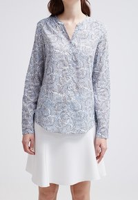 Langärmlige Bluse mit Knopfleiste in Hellblau mit geometrischem Muster, V-Ausschnitt und strukturierter Stoffqualität.