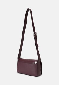 Borsa a tracolla in pelle bordeaux con design piatto, tracolla regolabile e accenti metallici. Presenta una parte superiore arrotondata e superficie lavorata.
