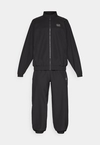 Ensemble de survêtement noir comprenant une veste zippée et un pantalon à taille élastique. Fabriqué en tissu lisse, avec un logo sur la poitrine et la cuisse, et des poignets côtelés.