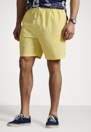 Pantaloni de baie galbeni, confecționați dintr-un material ușor, cu o talie elastică și șnur. Asociați cu pantofi din pânză bleumarin, având șireturi bej.