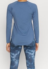 Helles blaues Langarmshirt mit Raglanärmeln, abgerundetem Saum und glatter Textur, kombiniert mit marineblauen Leggings im Batikdesign mit Wolkenmustern.