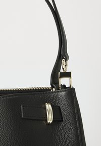 Black structured handbag with textured leather, gold hardware accents, and a zip closure. Features a short handle with a clip attachment.