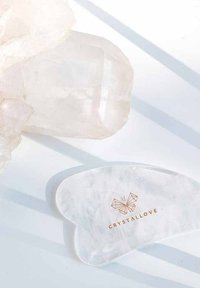 Gua sha-tool van rozenkwarts met een glad, hartvormig ontwerp. Heeft subtiele marmering en een gouden "CRYSTALLOVE"-logo.