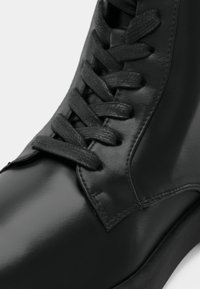 Botte noire en cuir lacée en gros plan mettant en valeur les lacets texturés et la surface lisse et polie.